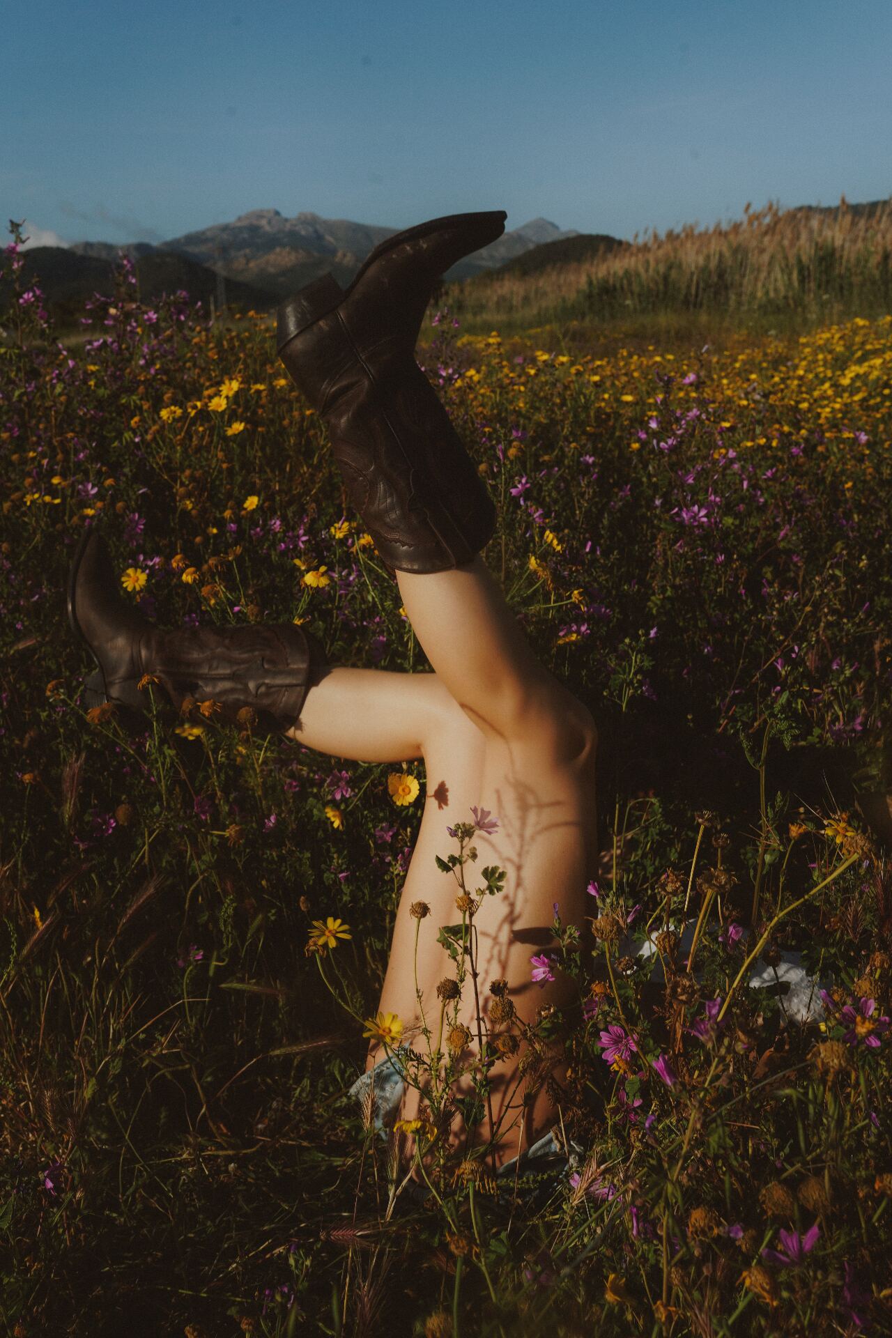 Legs in worn boots playfully kicked up in a field of yellow and pink wildflowers